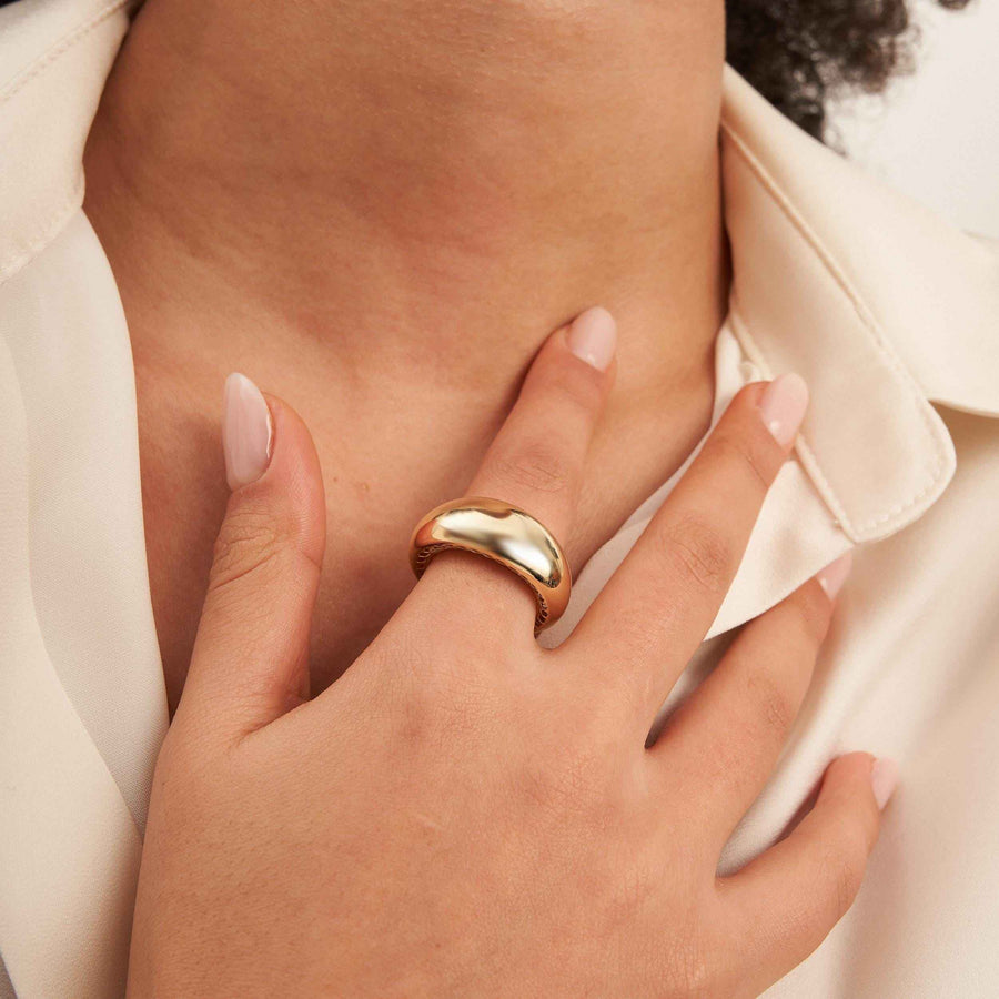 Anillo cúpula ancho en oro amarillo de 14 quilates puesto en el dedo, con la mano apoyada en el pecho