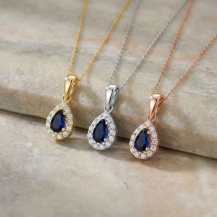 Gros plan de pendentifs halo saphir poire de synthèse en or jaune, blanc et rose 14 carats sur du marbre gris