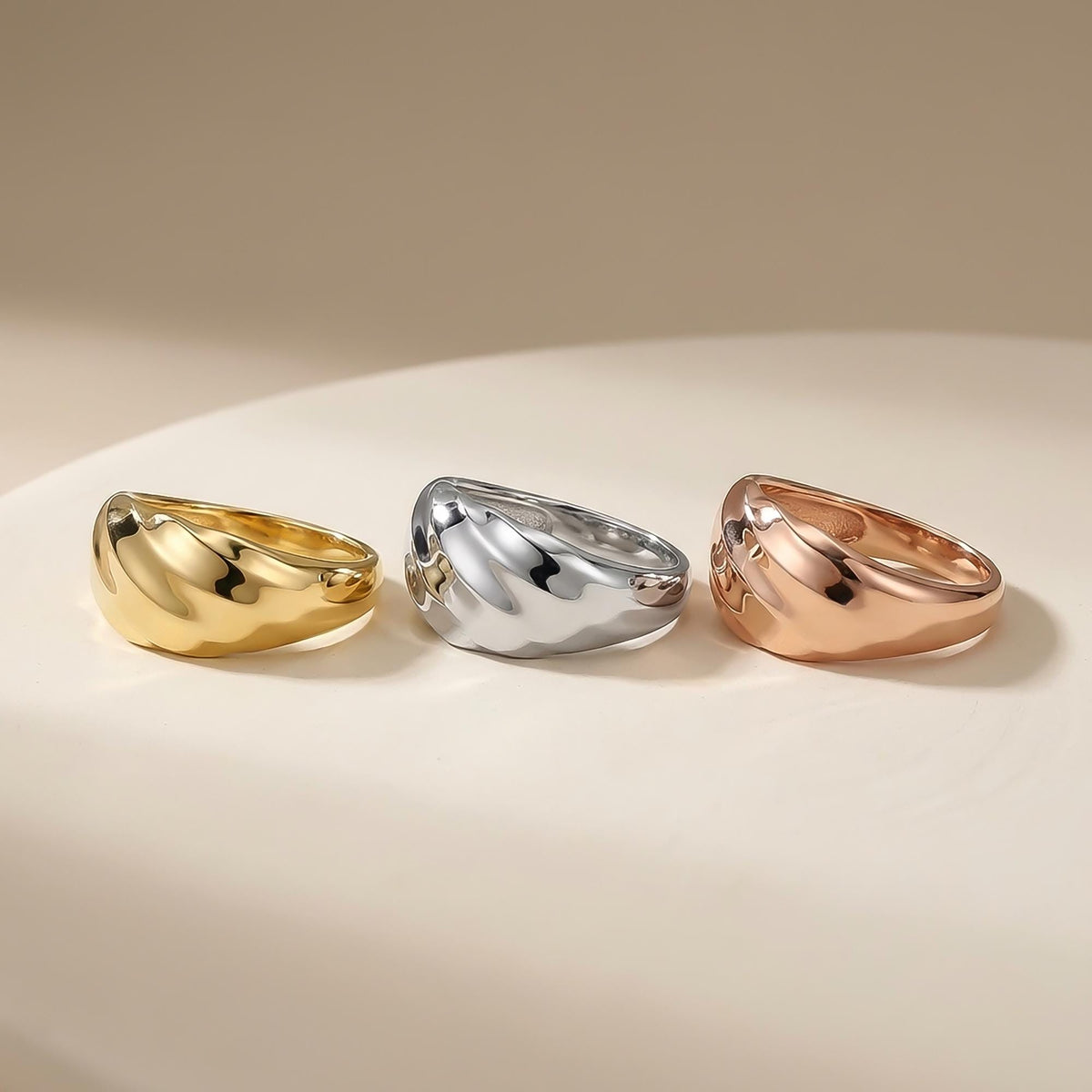 Swirl-Kuppelringe aus 585er Gelbgold, Weißgold und Roségold nebeneinander auf einem weißen Teller