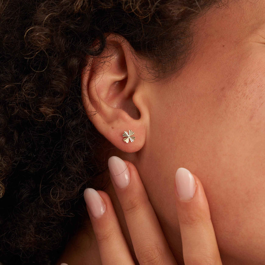 Primer plano de una oreja con un pendiente de botón de trébol diamantado en oro amarillo de 14 quilates