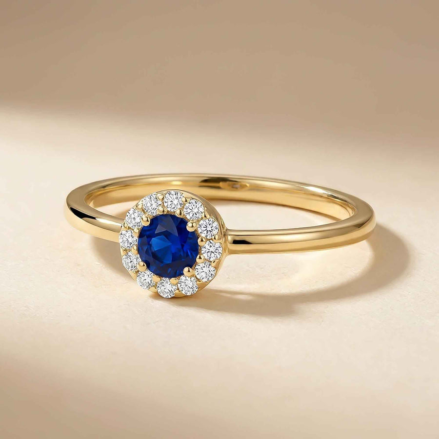 Bague halo saphir de synthèse en or jaune 14 carats inclinée sur fond beige