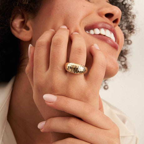 Modelo sonriente con la mano en la mejilla y un anillo cúpula diamantado en oro amarillo de 14 quilates
