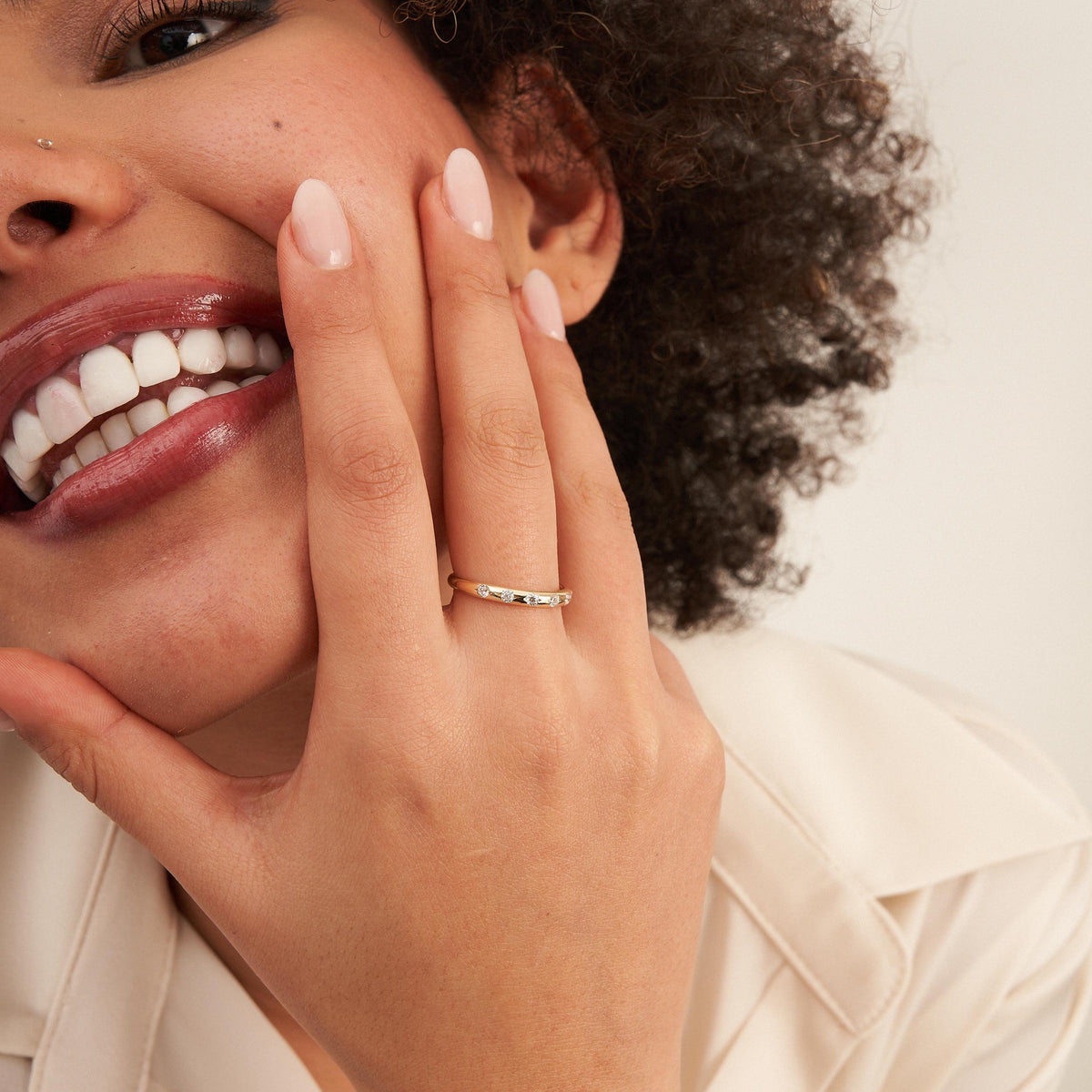 Smiling model with fingers at her cheek wearing a 14K yellow gold CZ band ring