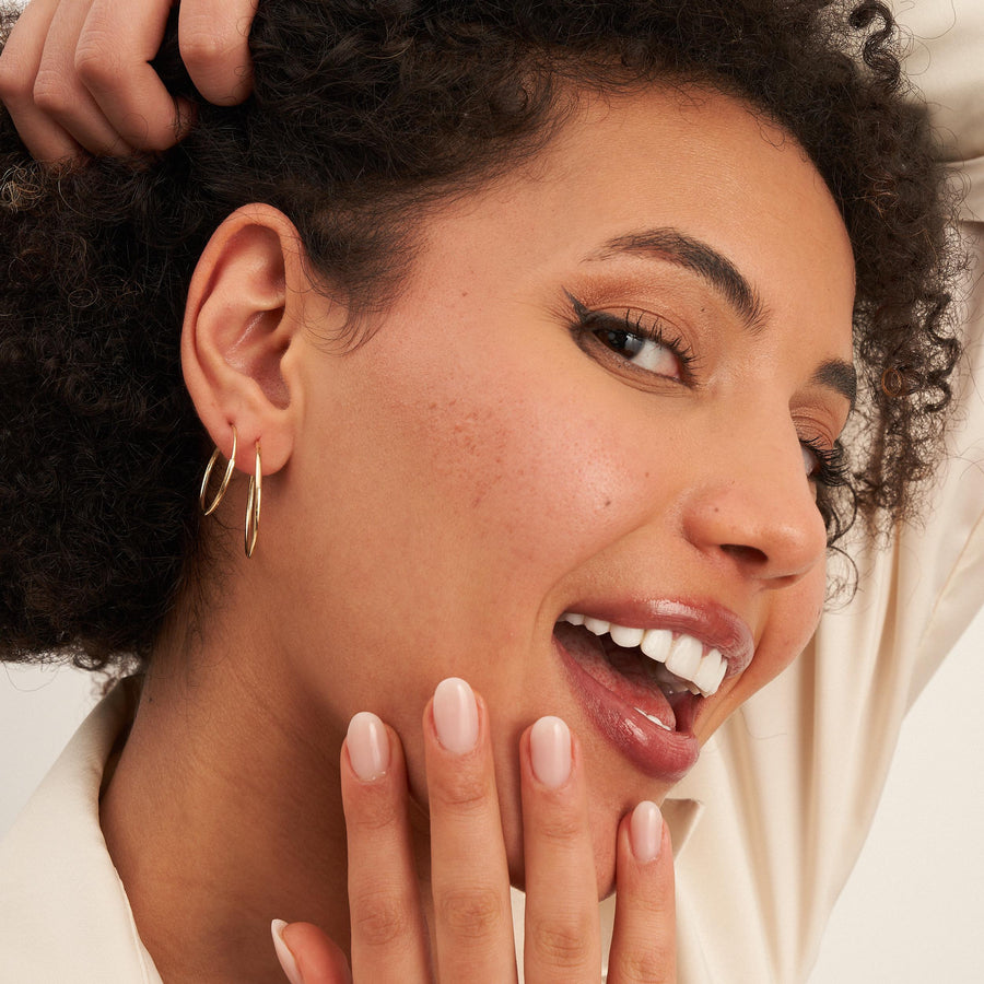 Modella che ride con le mani sul viso e indossa orecchini a cerchio endless in oro giallo 14kt