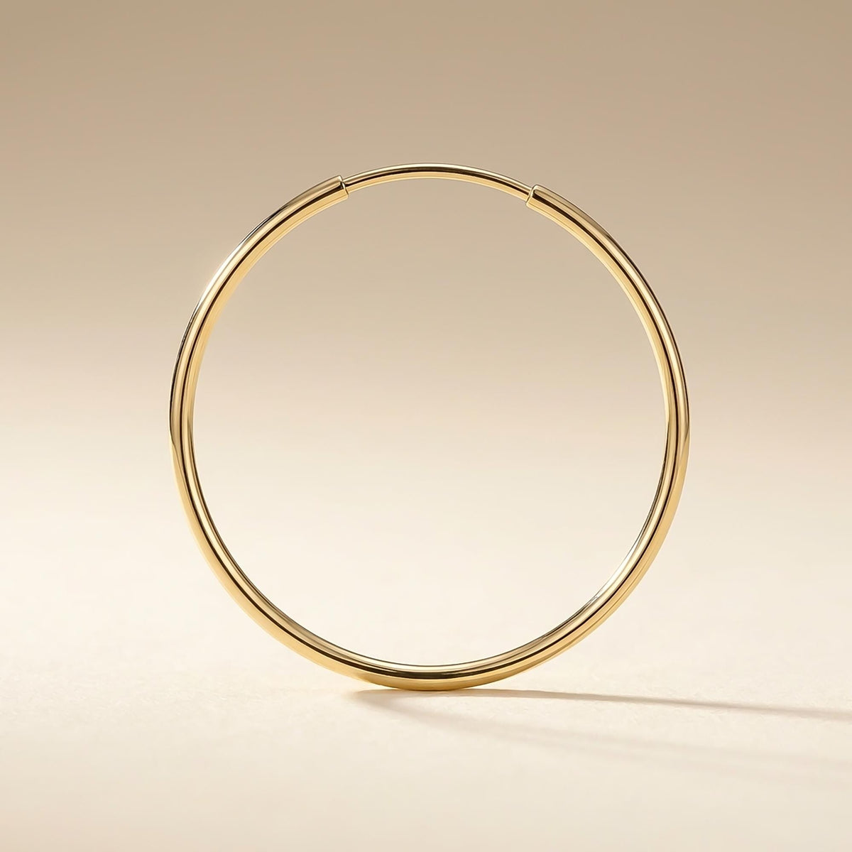 Singolo orecchino a cerchio endless in oro giallo 14kt posato in verticale su una superficie beige
