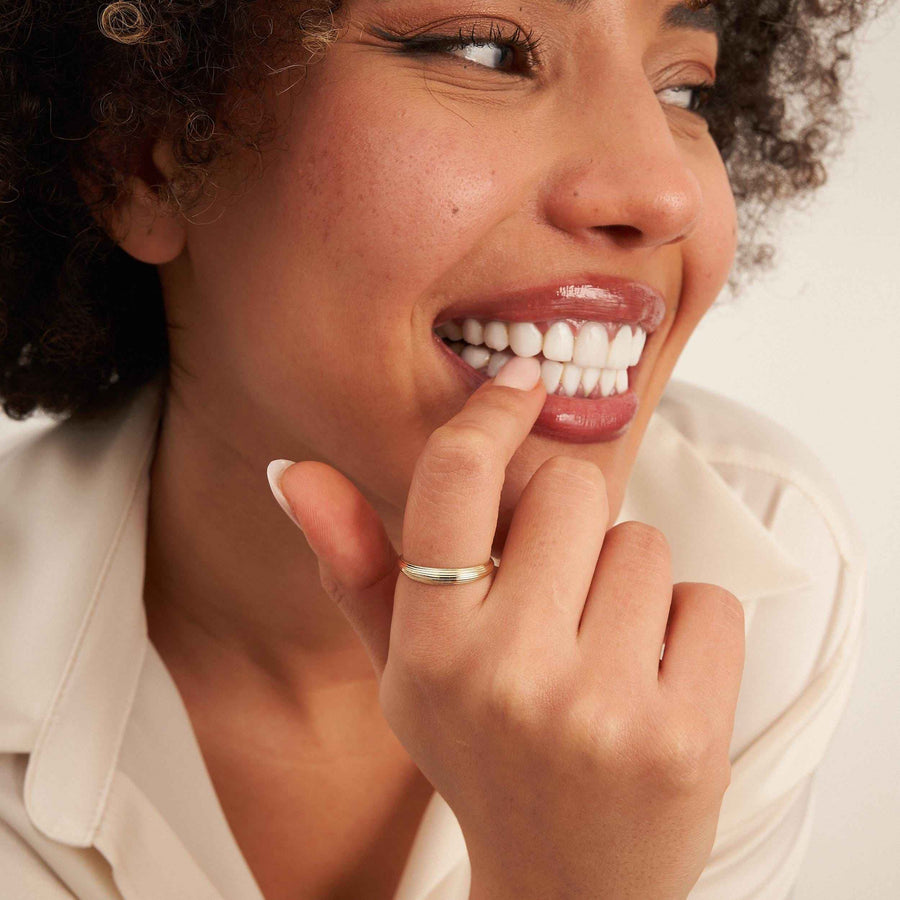 Modelo sonriente con un dedo en los labios y un anillo acanalado en oro amarillo de 14 quilates