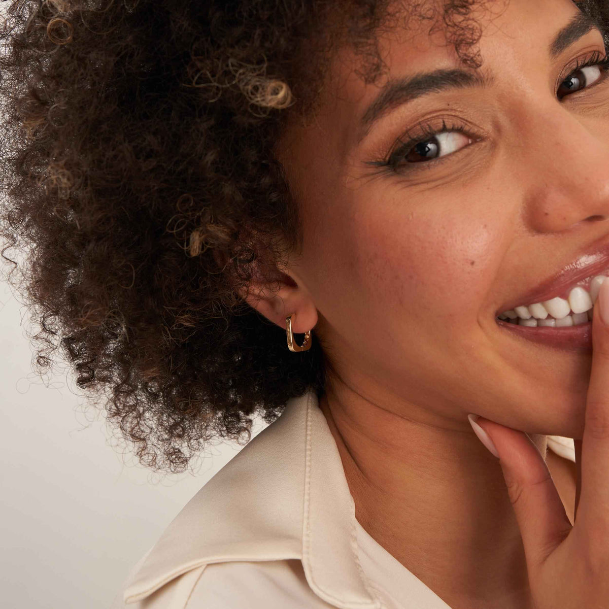 Smiling model with finger at lip wearing 14K yellow gold square hoop earrings
