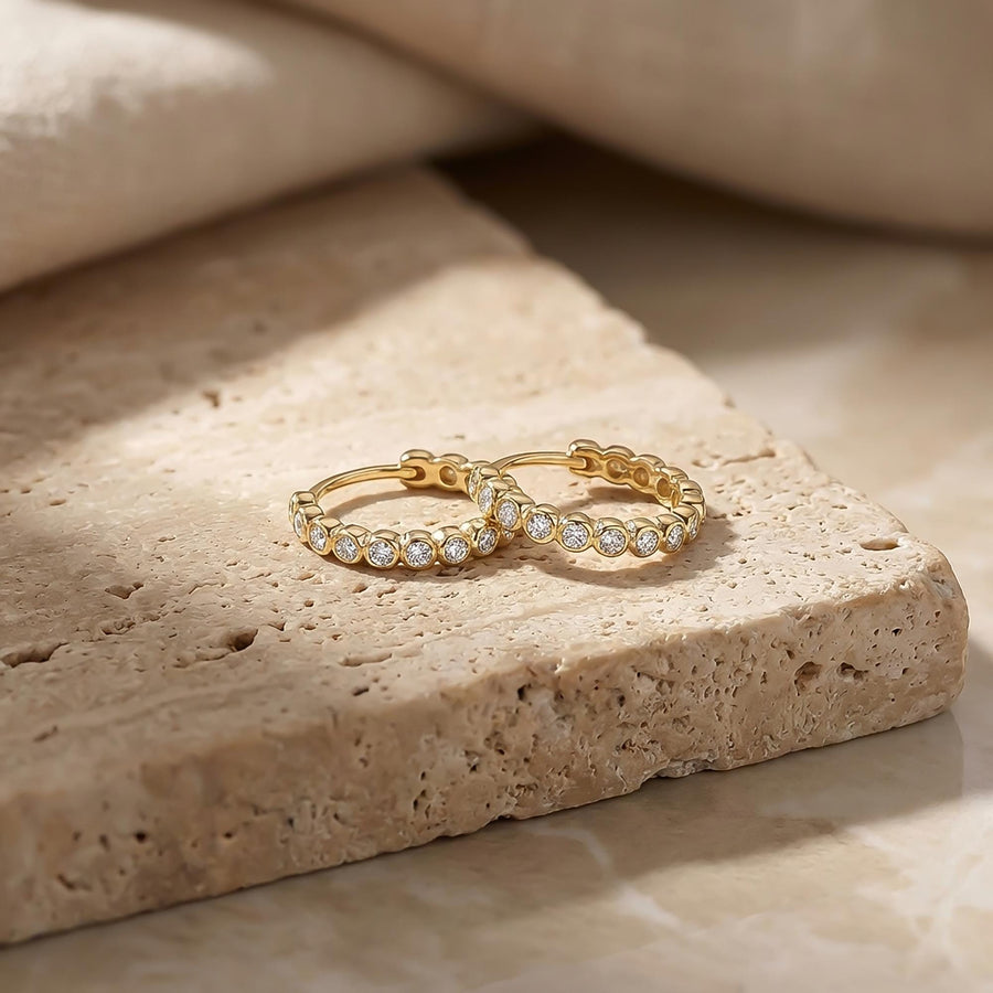 Paire de créoles à oxydes de zirconium en serti clos en or jaune 14 carats sur un bloc de travertin