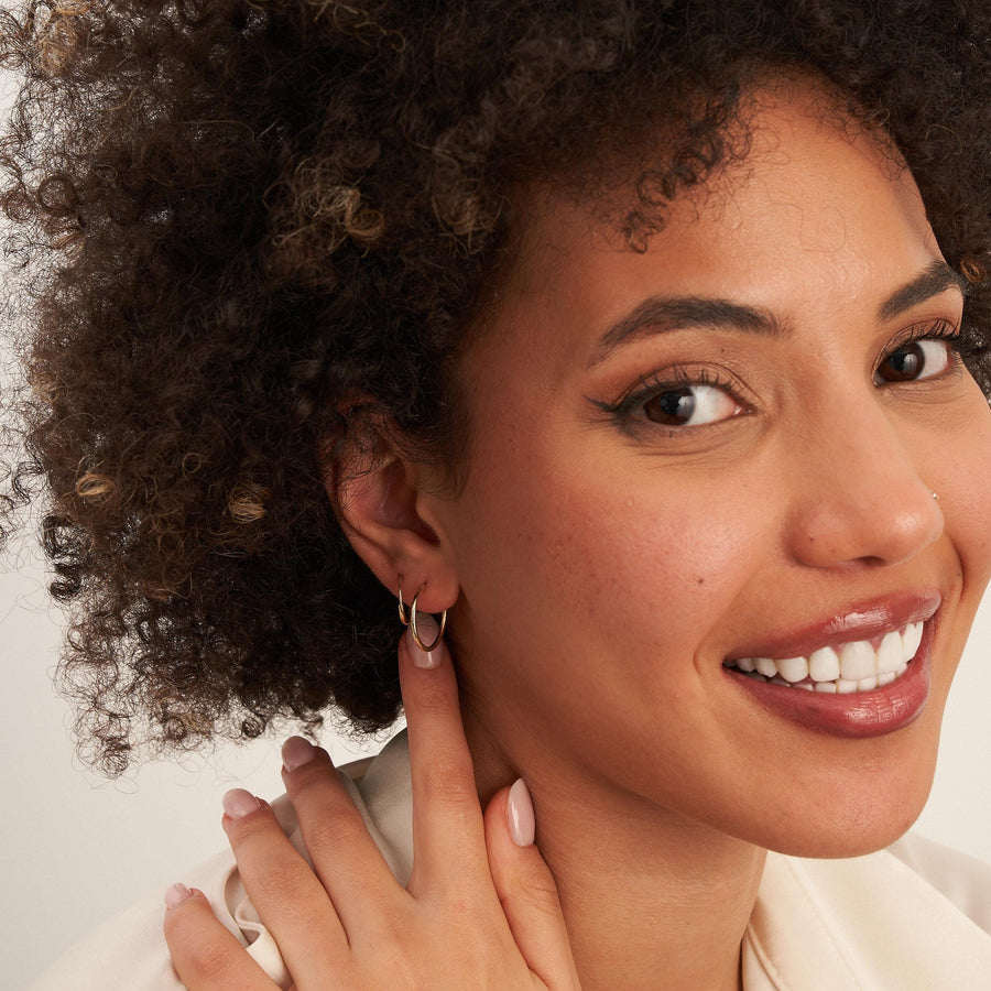 Modella sorridente con la mano sulla spalla che indossa orecchini a cerchio endless in oro giallo 14kt