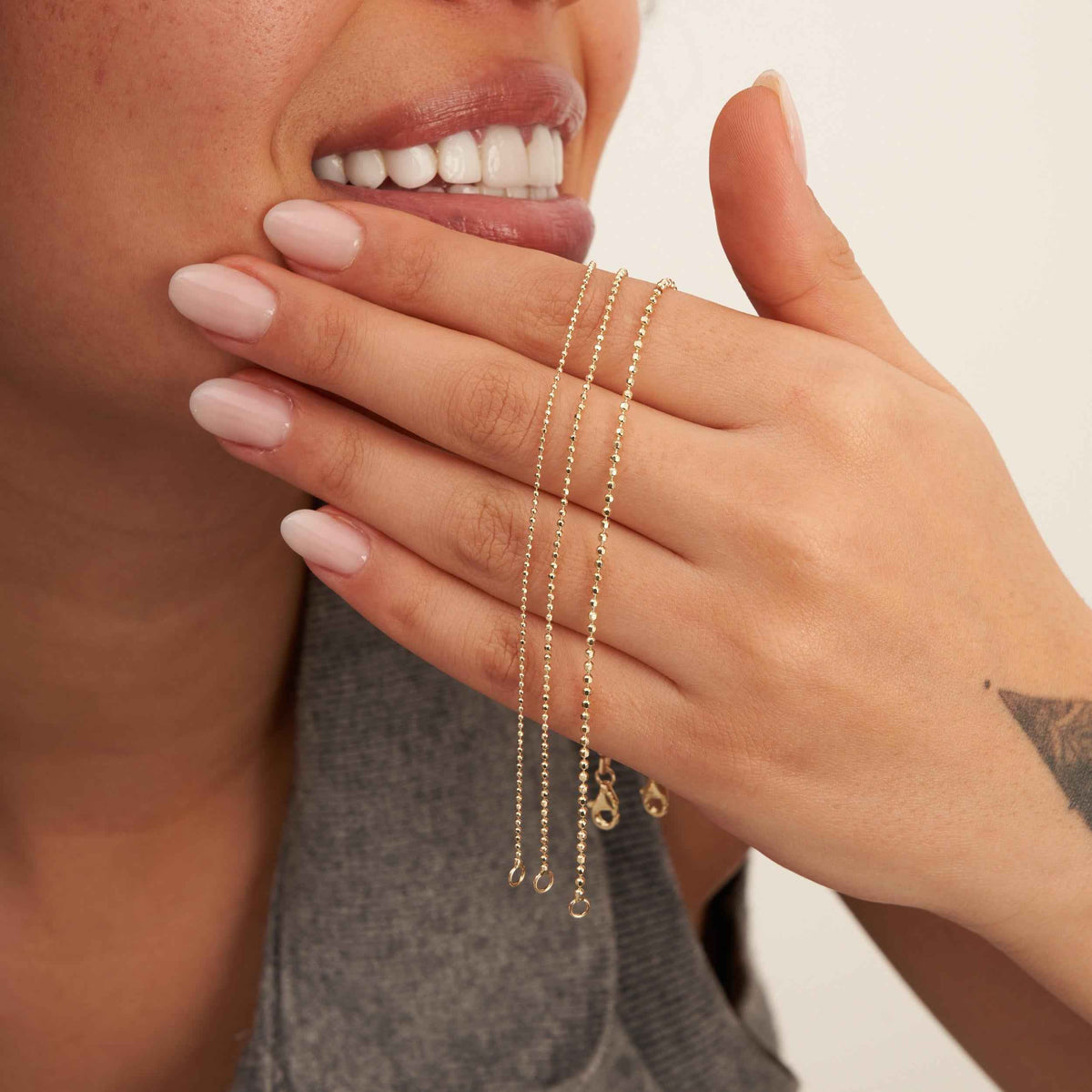 Pulseras de cadena de bolitas en oro amarillo de 14 quilates en la mano de la modelo, junto a su sonrisa