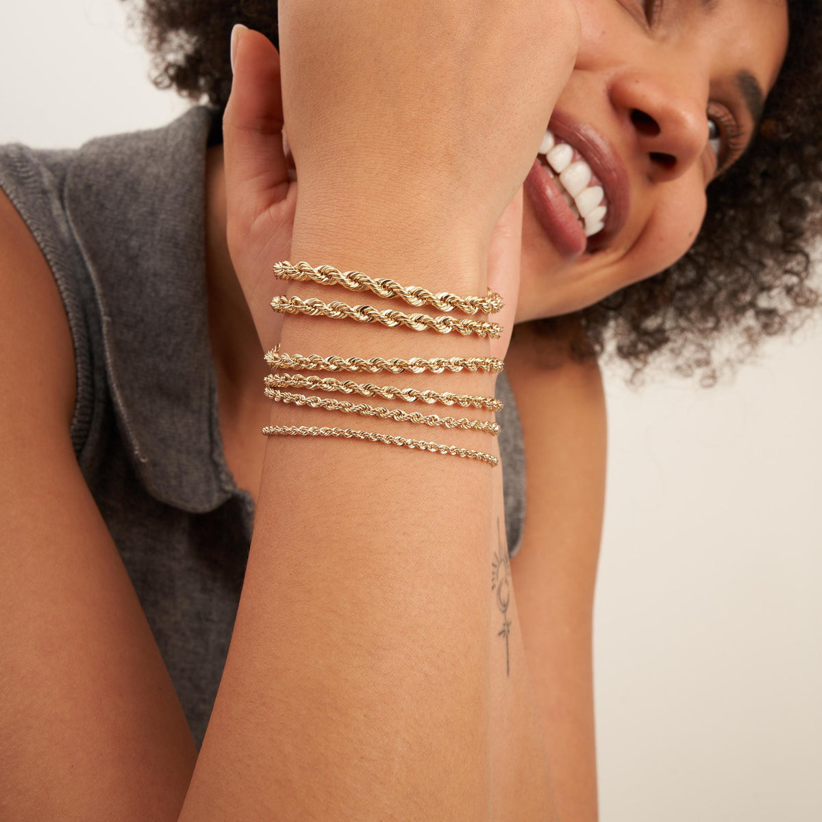 Modella sorridente con bracciali a corda in oro giallo 14kt sovrapposti al polso alzato