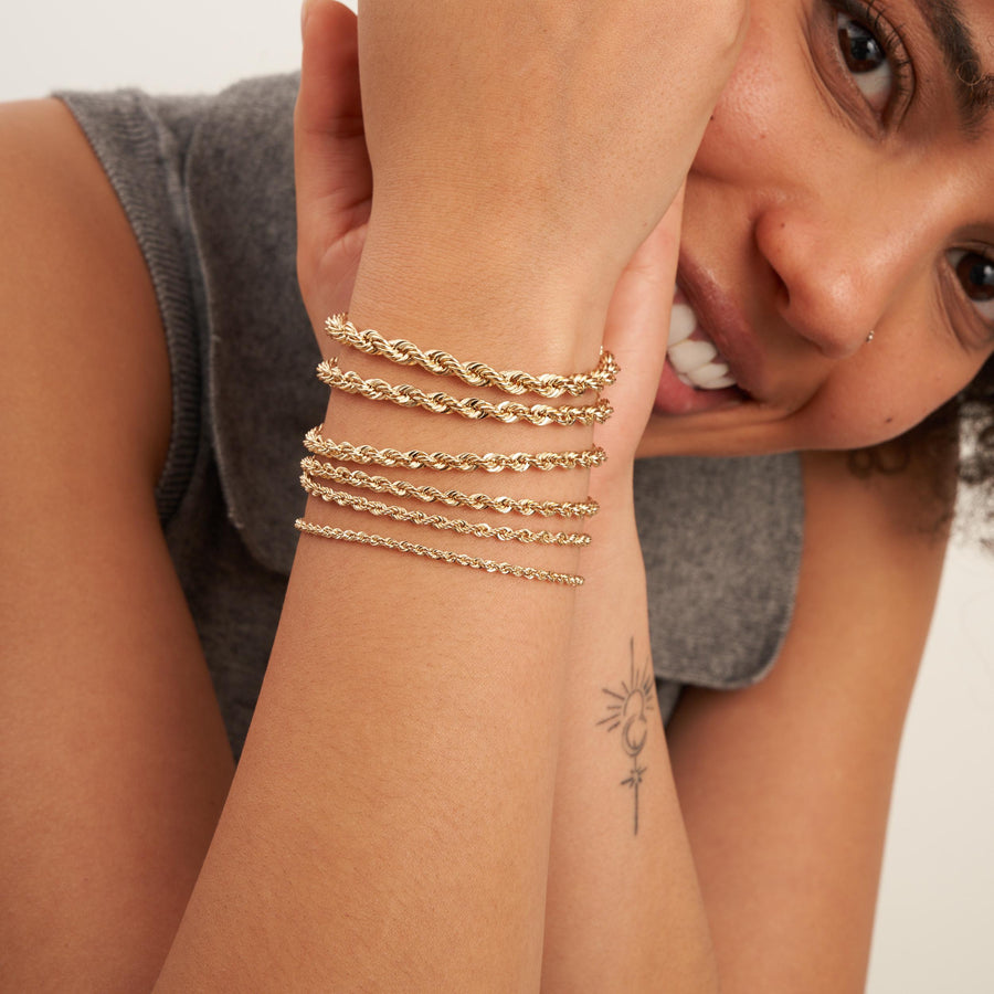 Modella sorridente con bracciali a catena a corda in oro giallo 14kt sovrapposti
