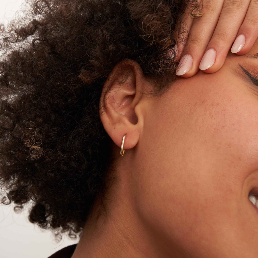 Gros plan d'une oreille, main sur le front, montrant une créole ovale fine en or jaune 14 carats