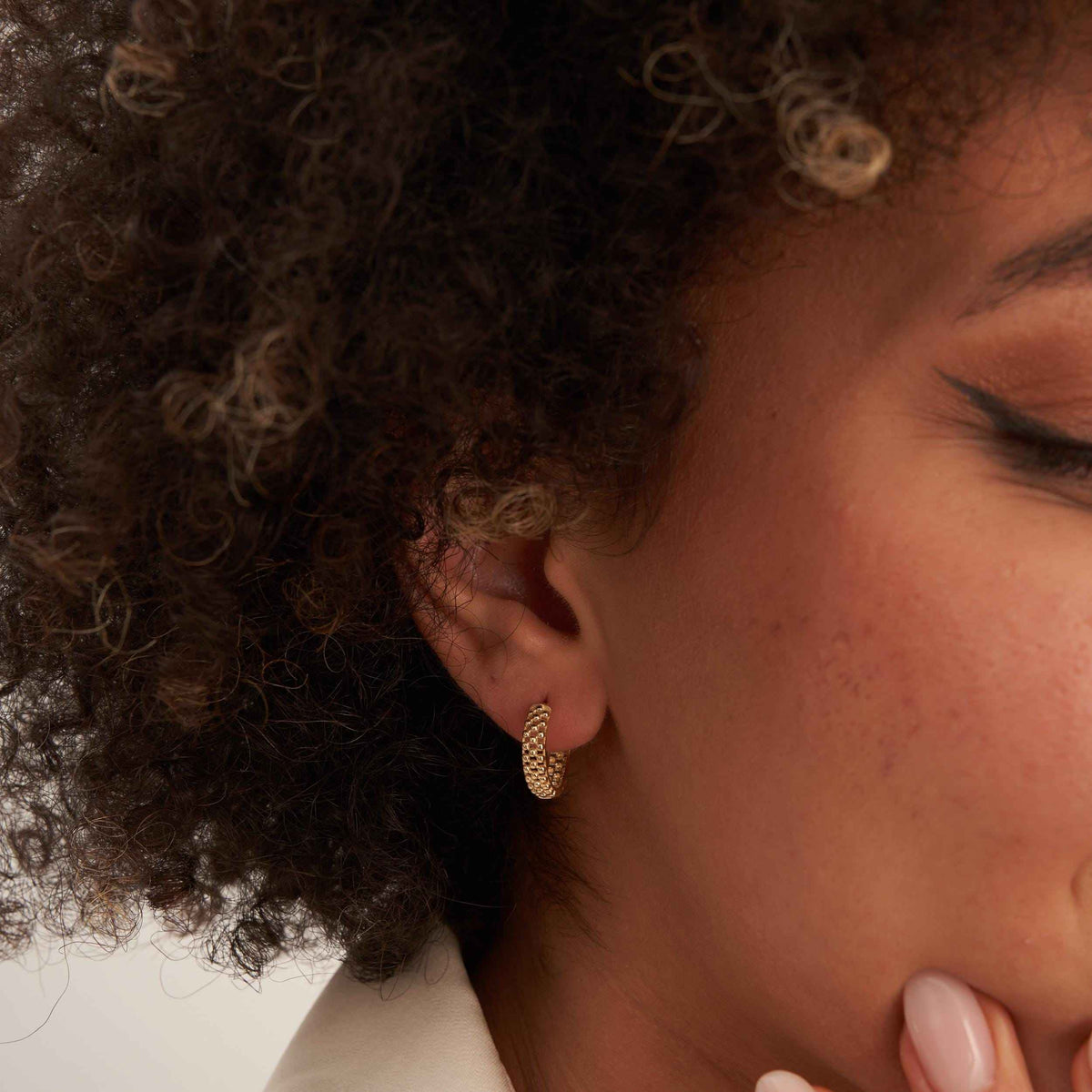 Gros plan sur l'oreille, les yeux fermés, avec une créole pointillée en or jaune 14 carats