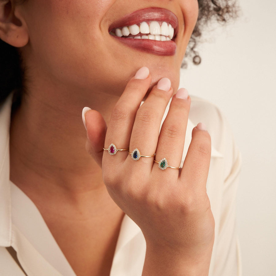 Close-up of 14K yellow gold pear halo rings on model's hand near her smile