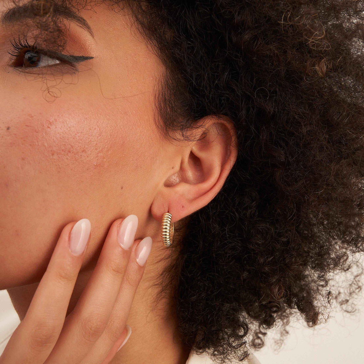 Model mit Hand an der Wange trägt gerippte Croissant-Creolen aus 585er Gelbgold