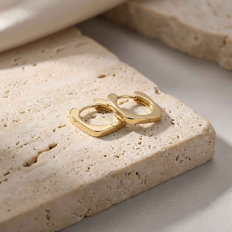 Pair of 14K yellow gold square hoop earrings on travertine stone