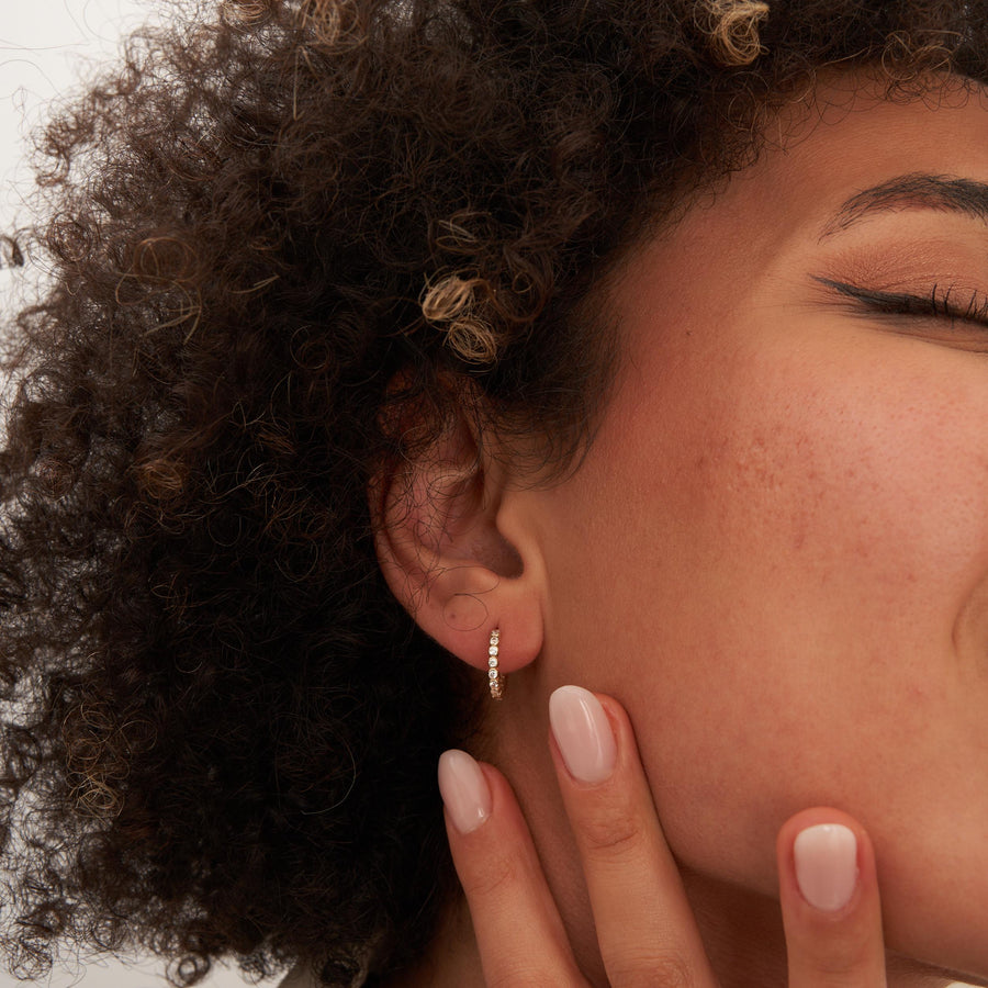 Gros plan sur l'oreille, les yeux fermés et la main à la mâchoire, créole à oxydes de zirconium en serti clos en or jaune 14 carats