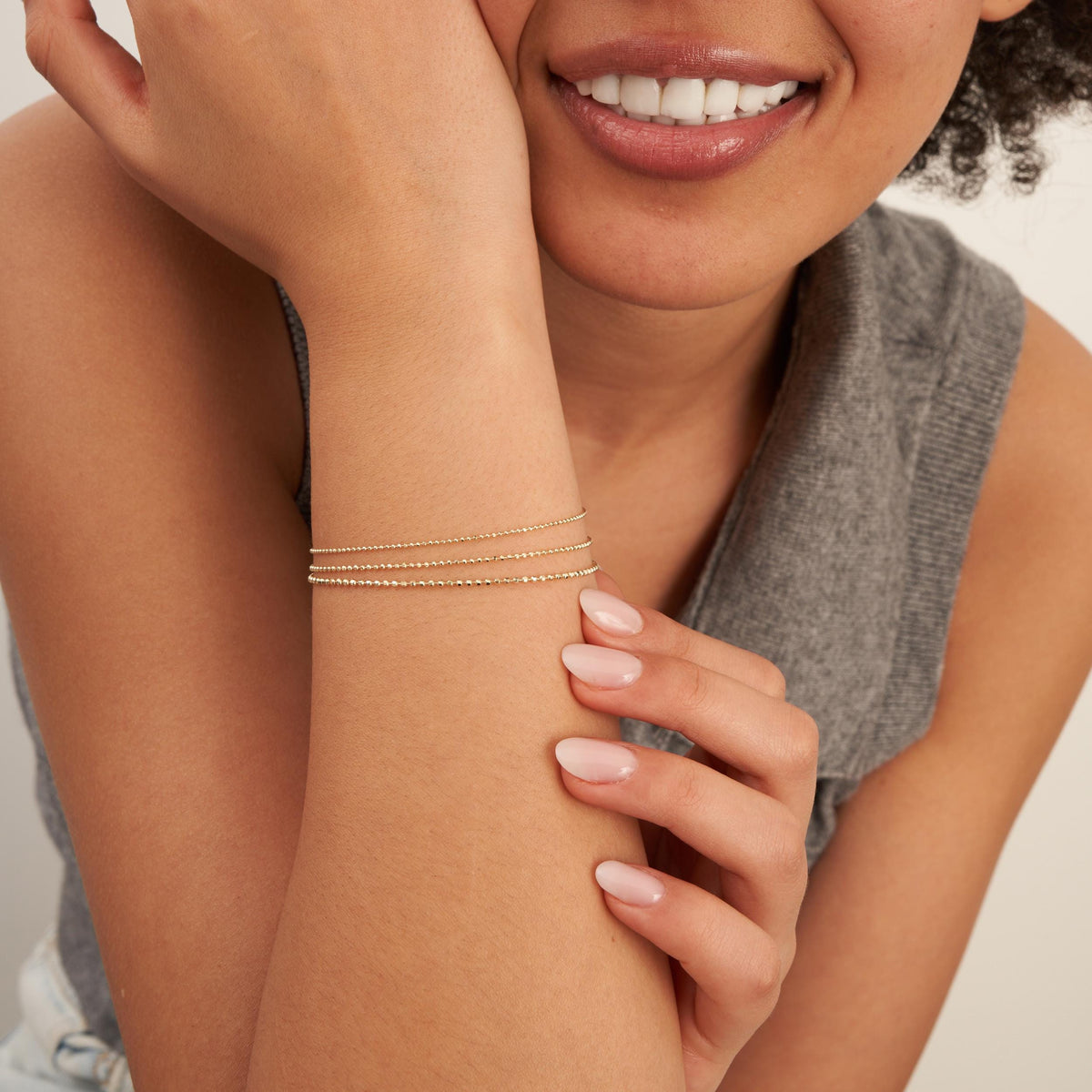Pulseras de cadena de bolitas en oro amarillo de 14 quilates llevadas por la modelo sonriente