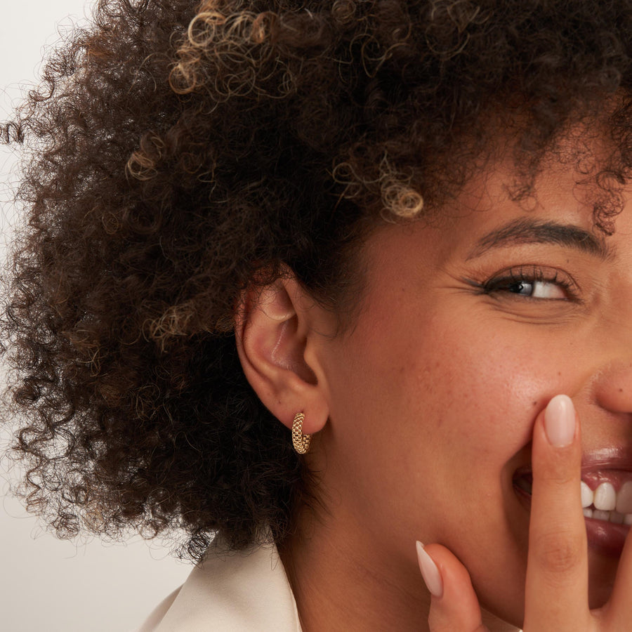 Créoles pointillées en or jaune 14 carats portées par un mannequin souriant, la main devant la bouche