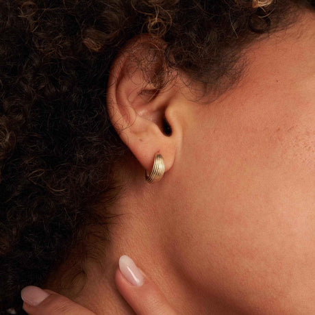 Créole cannelée en or jaune 14 carats portée au lobe, la main sur le cou