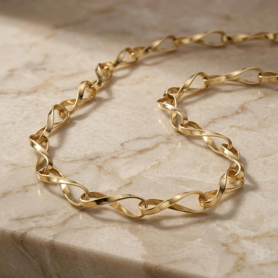 Collana a catena con maglia infinito ritorta in oro giallo 14kt adagiata sul marmo, dettaglio delle maglie