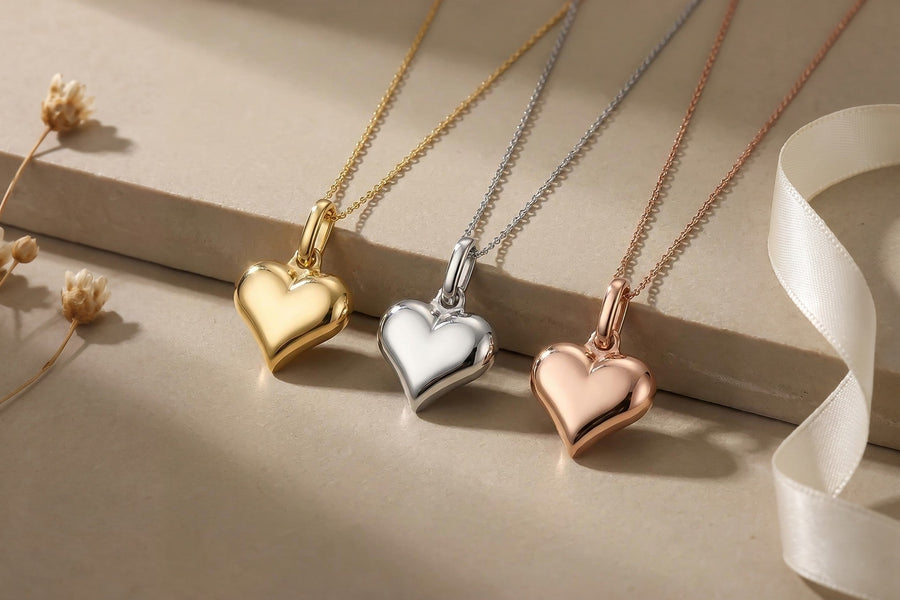 Heon 14K yellow, white and rose gold puffed heart necklaces on a stone ledge with an ivory silk ribbon