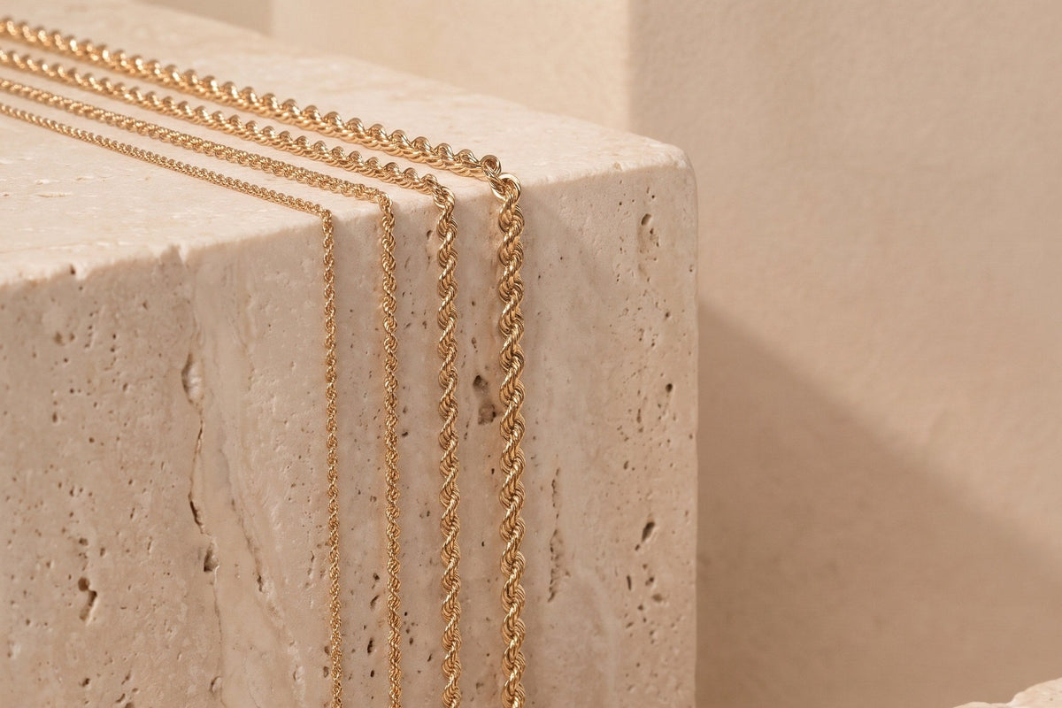 Four Heon 14K gold rope chains in different widths draped over travertine stone