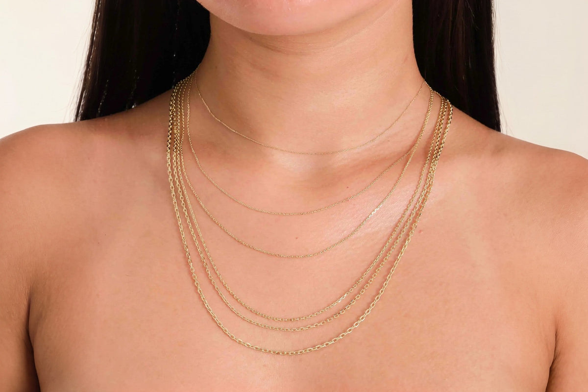 Five Heon 14K yellow gold diamond-cut cable chains layered in graduated lengths on the neck