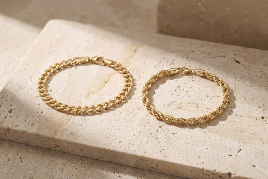 Heon 14K gold Cuban link bracelet and rope chain bracelet side by side on travertine