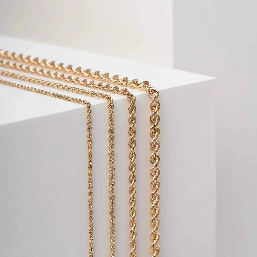 Side view of 14K yellow gold rope chain necklaces hanging over white display block