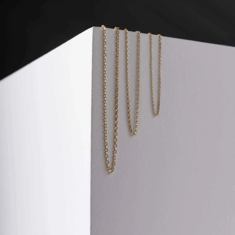 Chaînes maille forçat taille diamant en or jaune 14 carats drapées sur un présentoir blanc