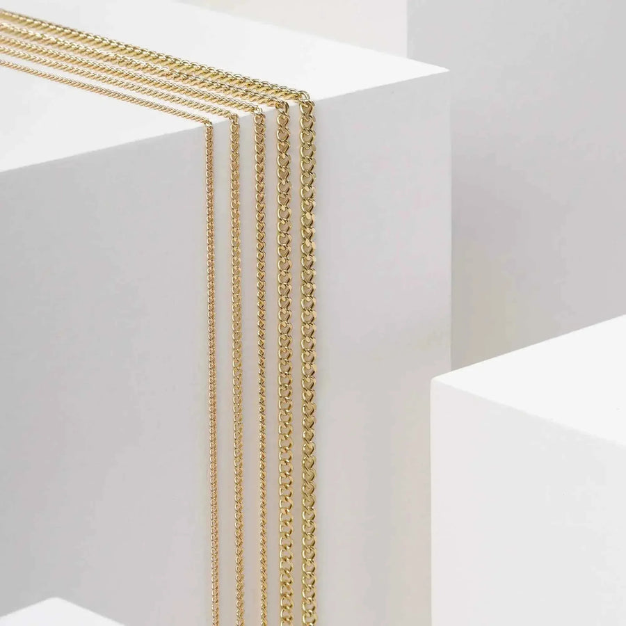 Vista lateral de cadenas cubanas Miami en oro amarillo de 14 quilates colgadas de un expositor blanco