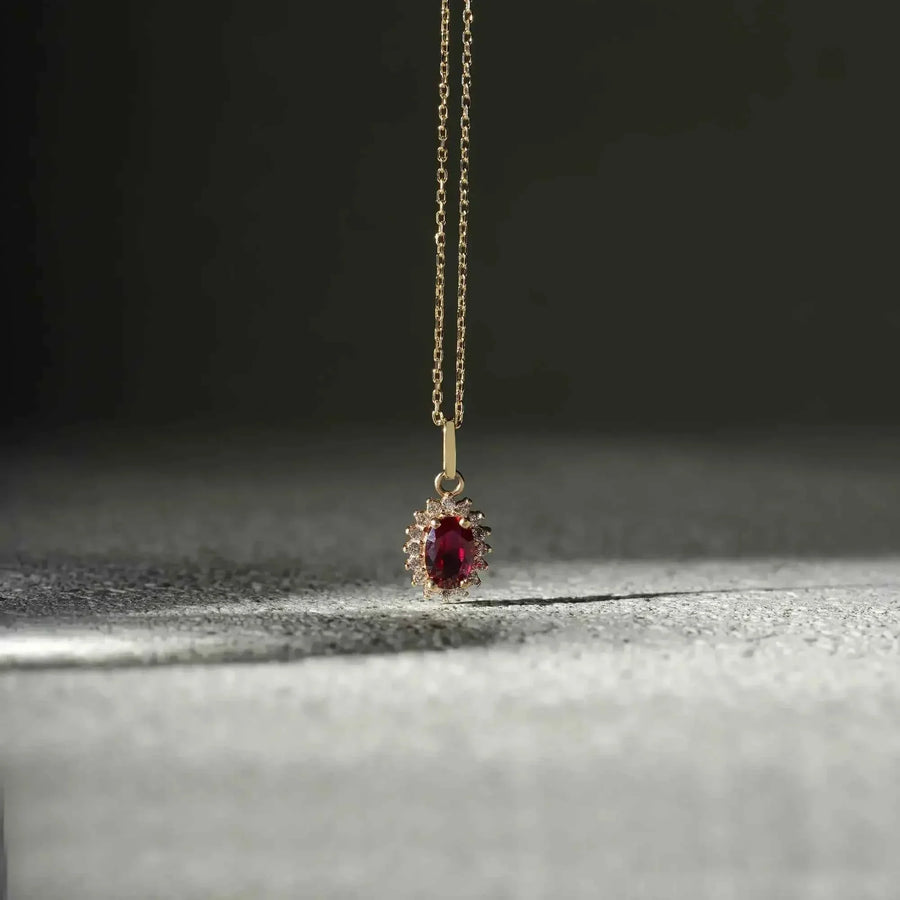 Collier pendentif halo rubis de synthèse en or jaune 14 carats suspendu au-dessus d'une surface sombre texturée