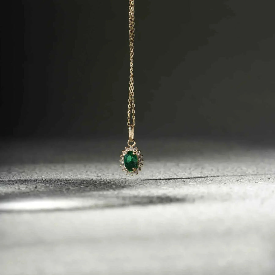 Collana con ciondolo halo in oro giallo 14kt con smeraldo creato in laboratorio, sospesa su una superficie scura texturizzata