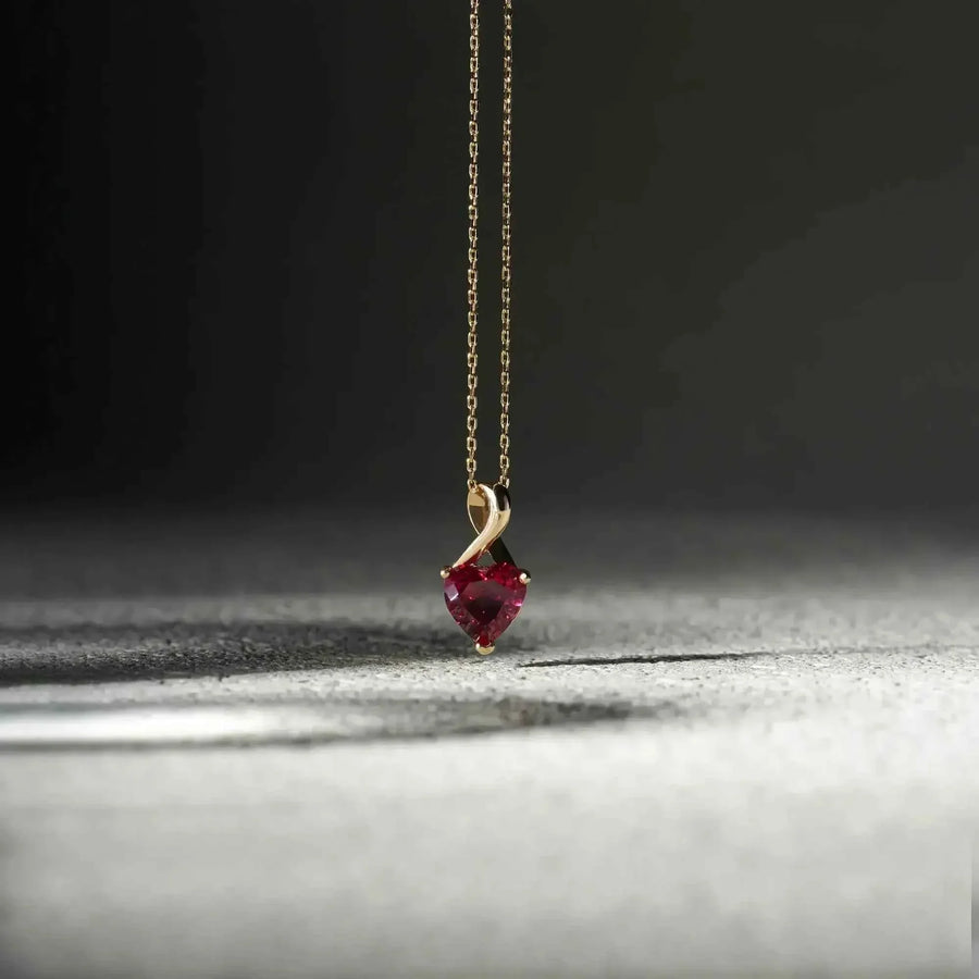 Collana con ciondolo cuore in oro giallo 14kt con rubino creato in laboratorio, sospesa su una superficie grigia texturizzata