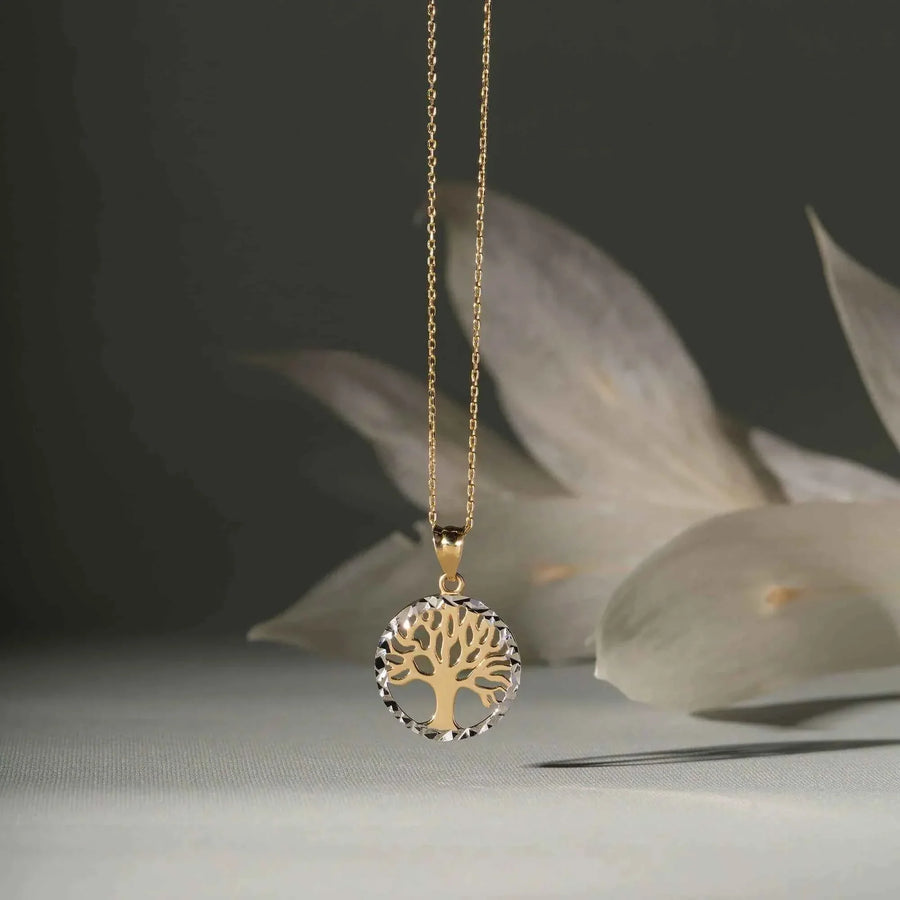 Collier pendentif arbre de vie bicolore en or 14 carats suspendu sur fond sombre avec des feuilles