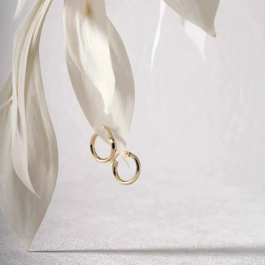 Dos pendientes de aro clásicos pequeños en oro amarillo de 14 quilates enlazados, apoyados sobre una hoja clara