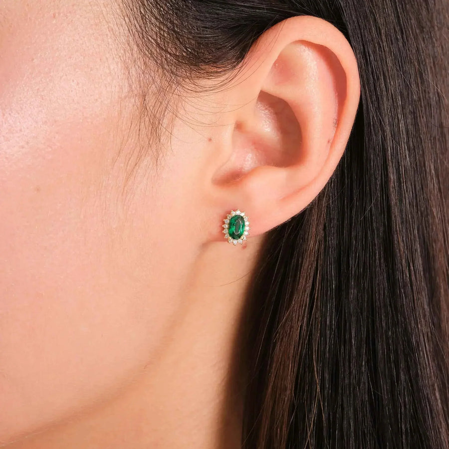 Gros plan d'une puce d'oreille halo émeraude de synthèse en or jaune 14 carats portée au lobe de l'oreille