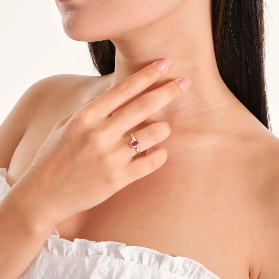 Bague pierre de naissance halo rubis de synthèse en or 14 carats portée sur une main qui touche le cou du mannequin