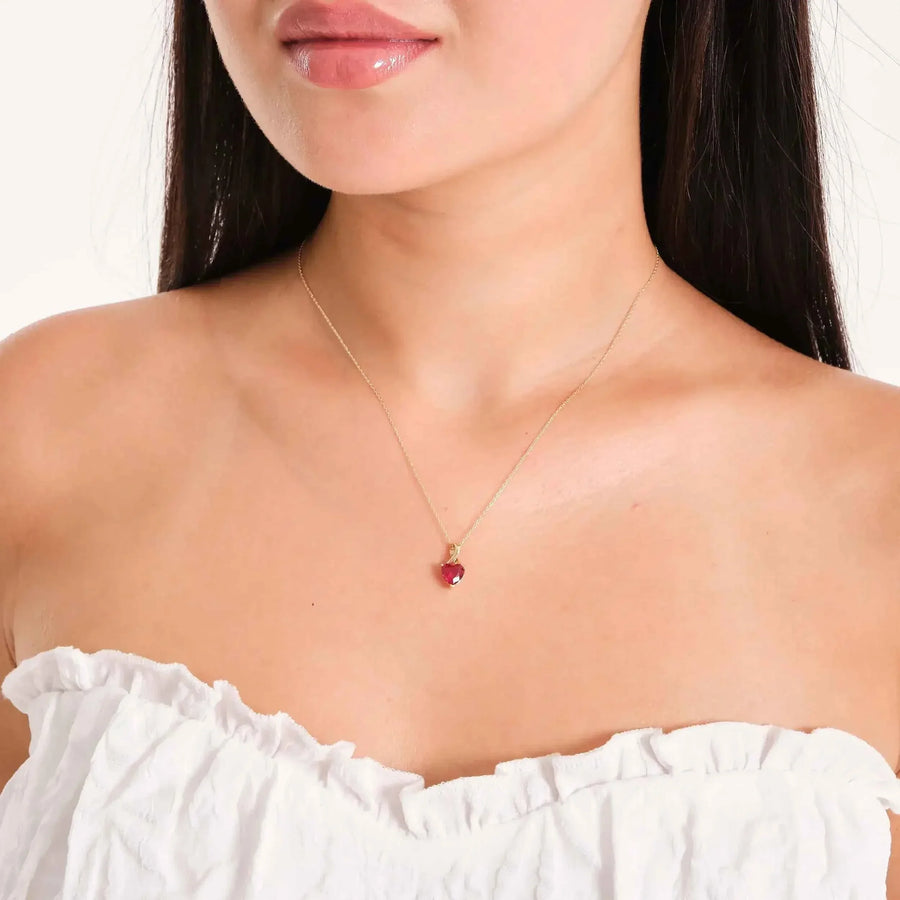 Collana con ciondolo cuore in oro giallo 14kt con rubino creato in laboratorio indossata da una modella con top bianco con volant