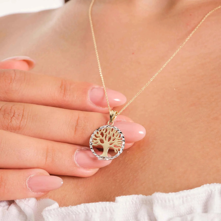 Gros plan du collier pendentif arbre de vie bicolore en or jaune et or blanc 14 carats tenu entre les doigts