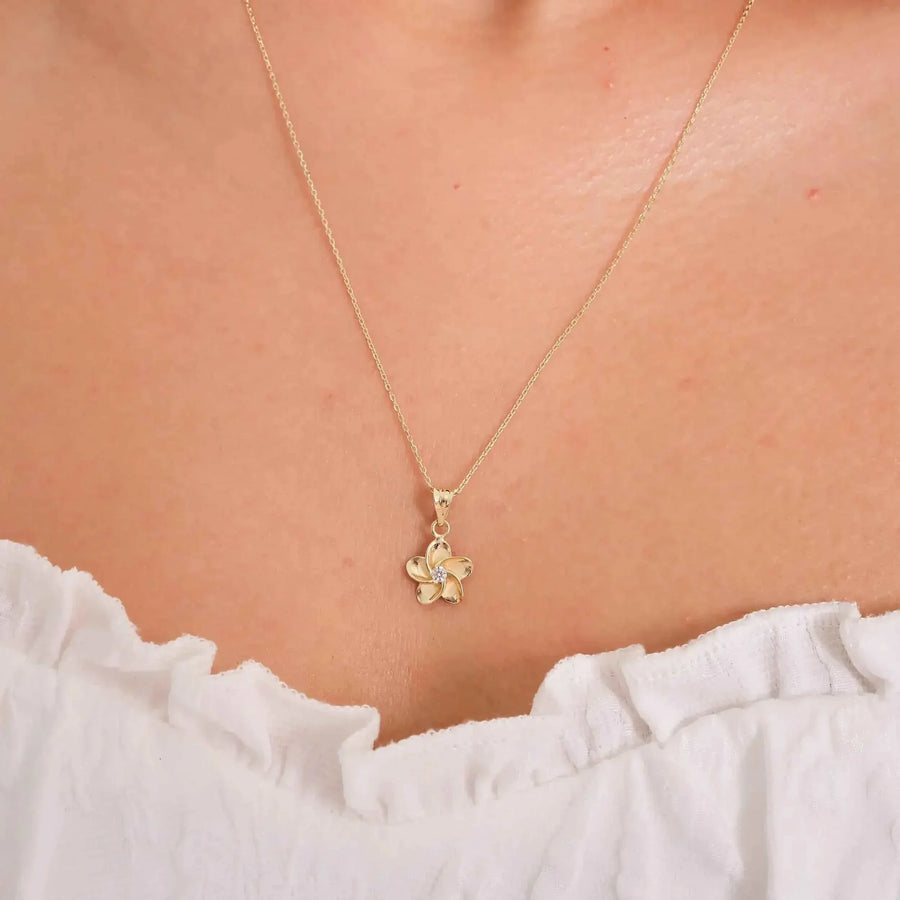 Gros plan du collier pendentif fleur de frangipanier en or jaune 14 carats porté au cou