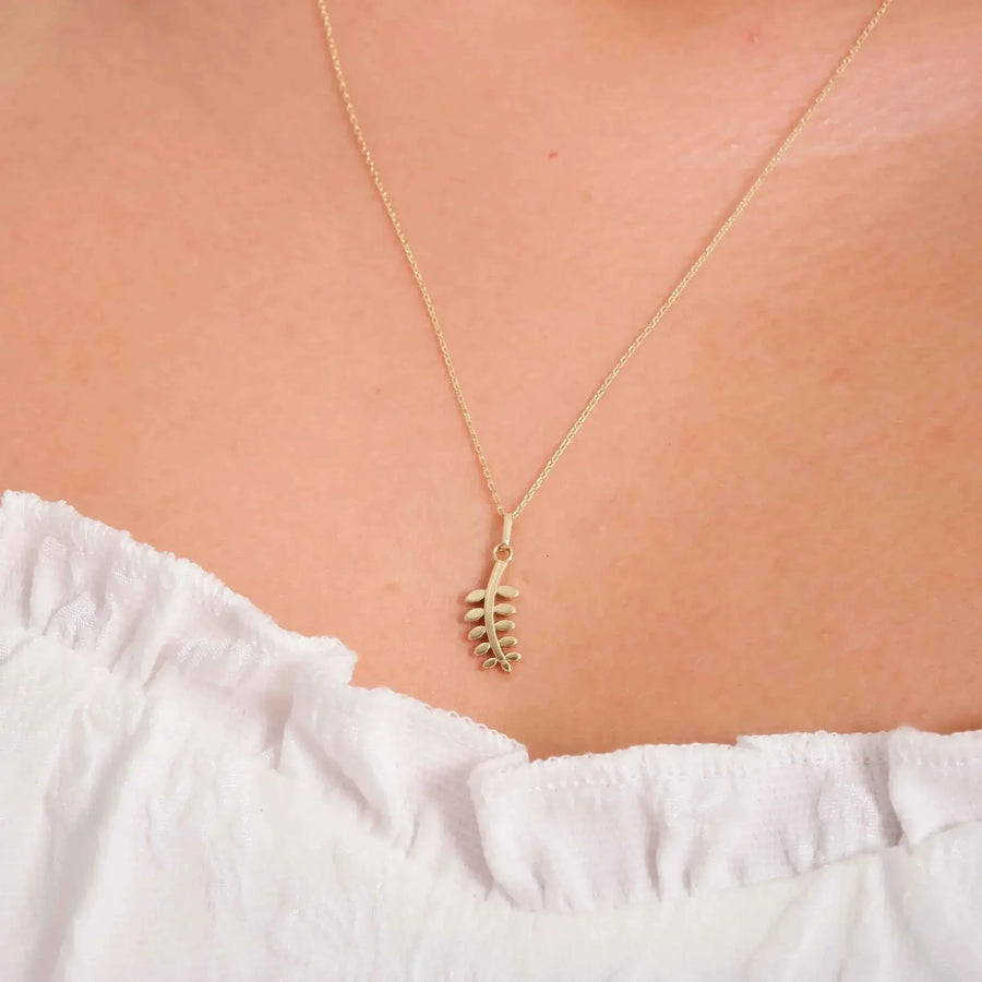 Gros plan du collier pendentif branche d'olivier en or jaune 14 carats porté au cou au-dessus d'un haut à volants