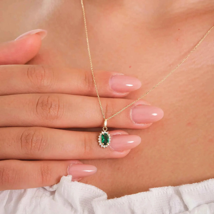 Collana con ciondolo halo in oro giallo 14kt con smeraldo creato in laboratorio tenuta tra le dita dalla modella