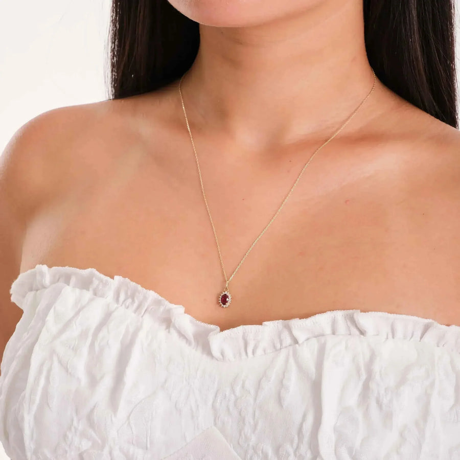 Collier pendentif halo rubis de synthèse en or jaune 14 carats porté par un mannequin en haut blanc à épaules dénudées