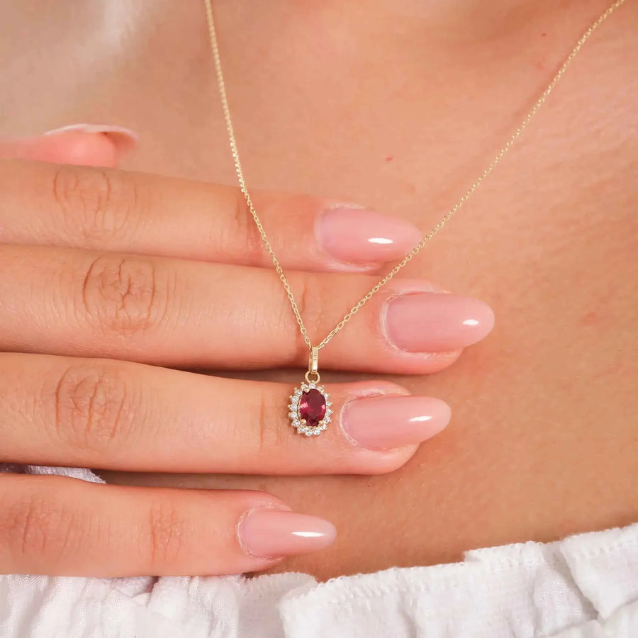 Collier pendentif halo rubis de synthèse en or jaune 14 carats porté et tenu entre les doigts