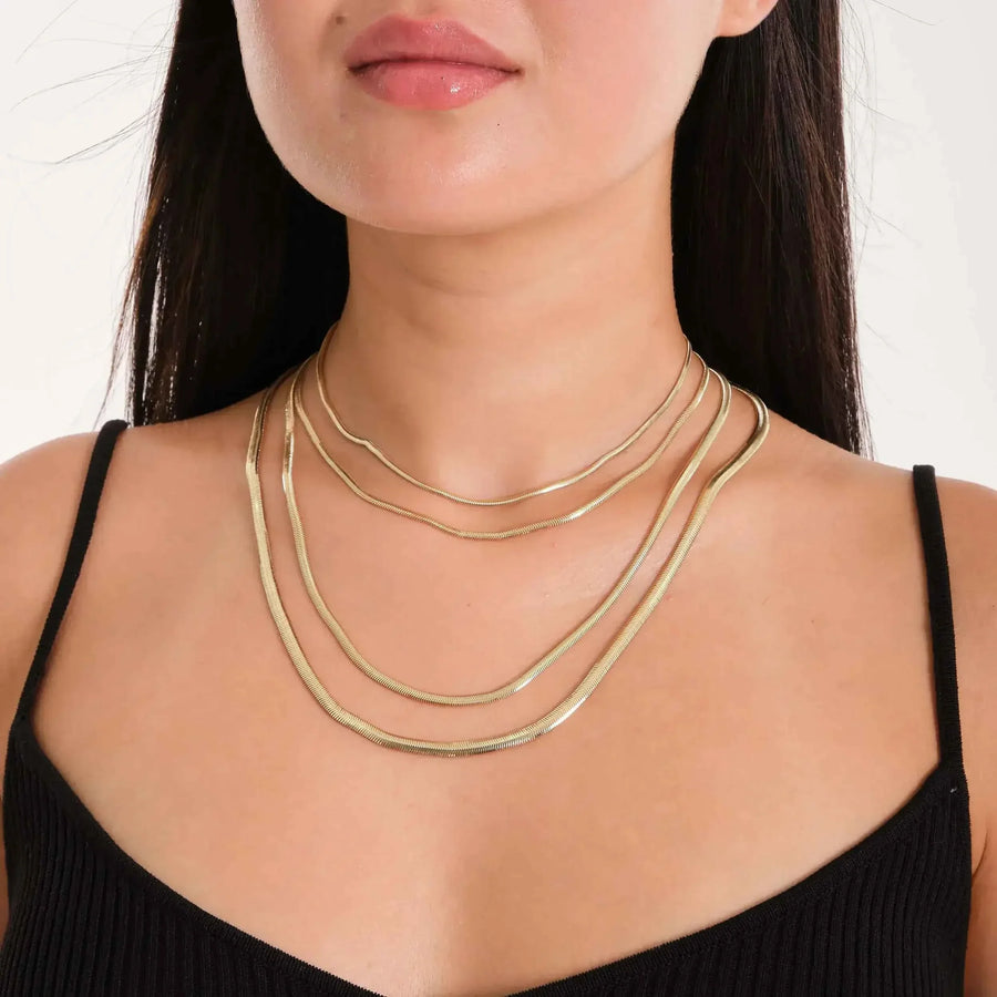 14K yellow gold flat herringbone chain necklaces layered on model in black top