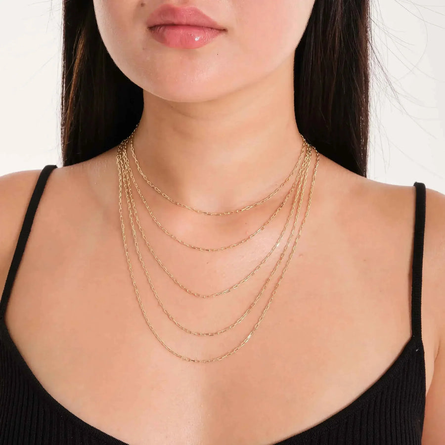Chaînes fines maille paperclip en or jaune 14 carats superposées, portées par un mannequin en haut noir