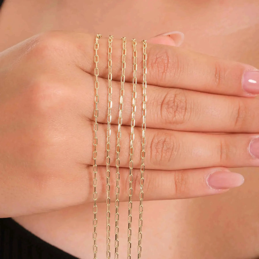 Chaînes fines maille paperclip en or jaune 14 carats drapées sur les doigts